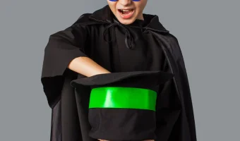 Copil costumat în magician, cu baghetă și joben.